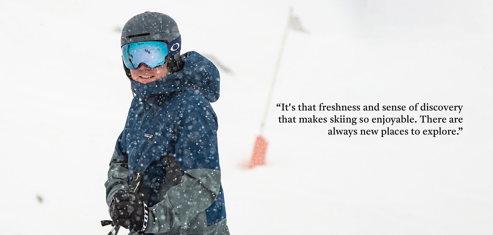 Skier wearing a ski jacket, helmet and goggles standing in side profile in a blizzard looking happy. 