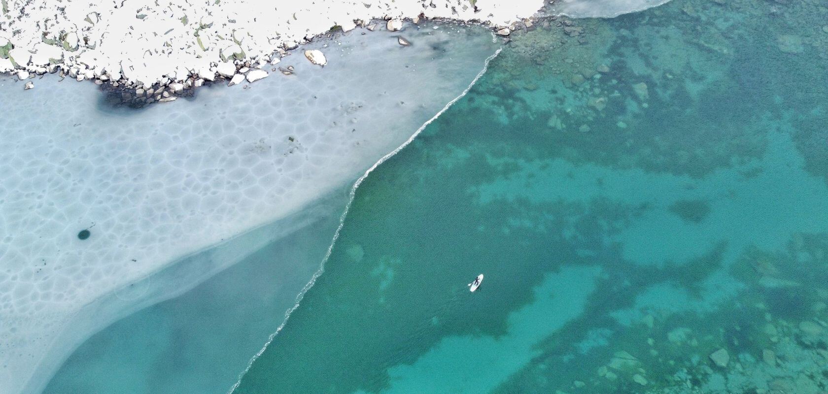 An areil shot of a person paddleboarding across a half frozen lake