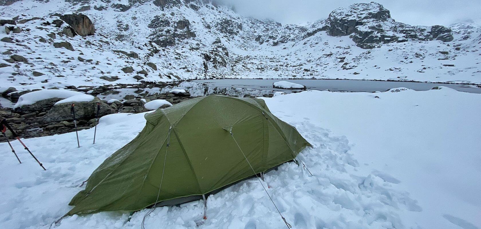 A tent pitched on the border of an alpine lake with snow coverage