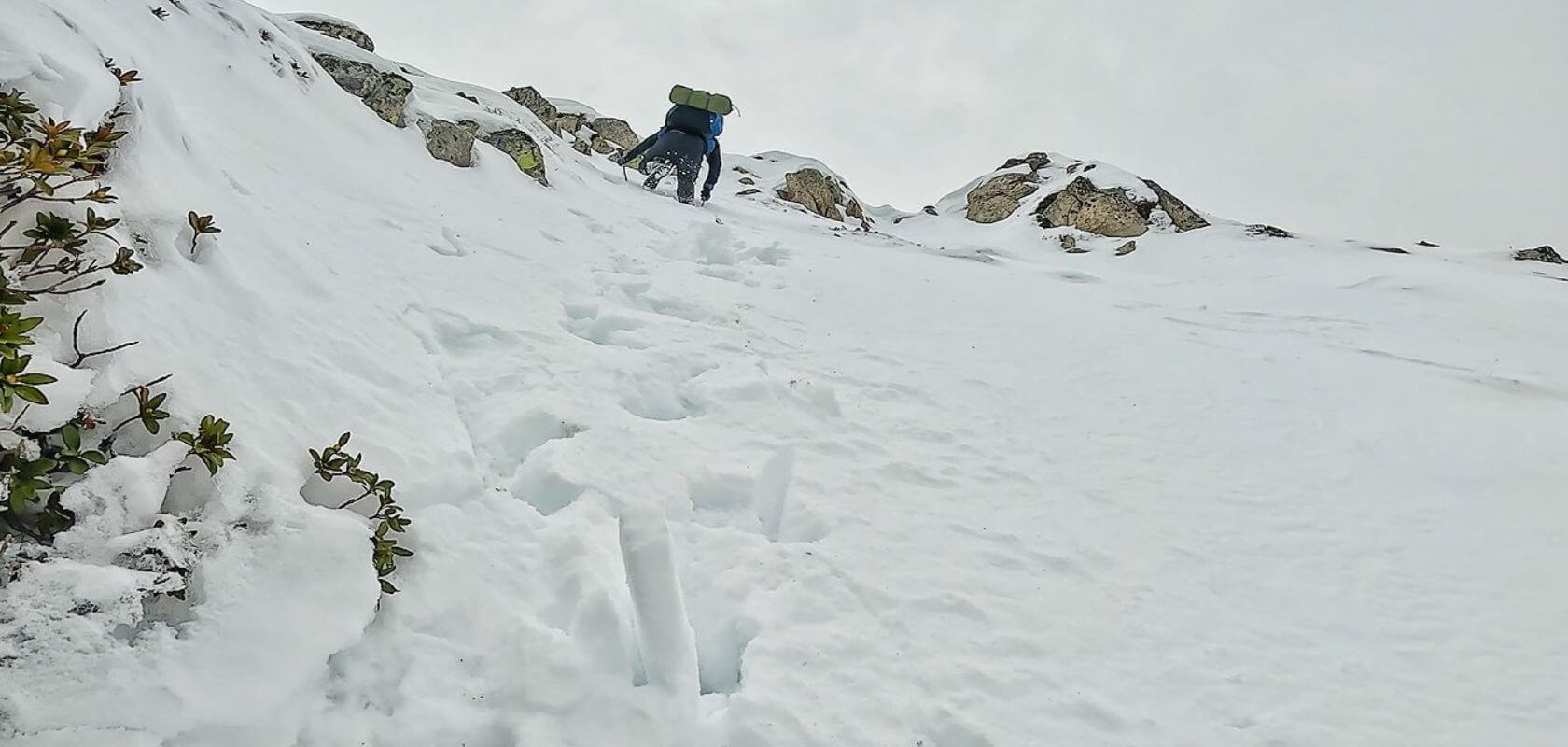 Person climbing up  steep snowy ridge.