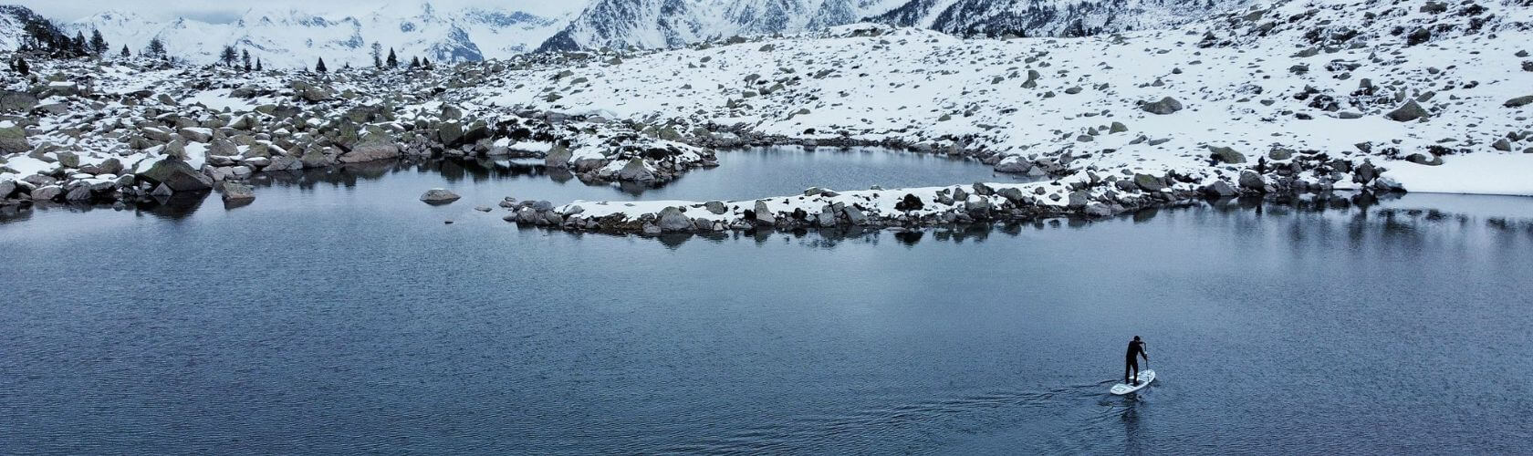 A man paddleboarding across a half frozen lake  