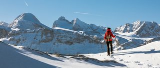 A woman is walking with snow shoes in fluffy powder snow in front of the Dachstein Mountains on a beautiful winterday. The region is famous for hiking, skiing,and climbing all over the year.