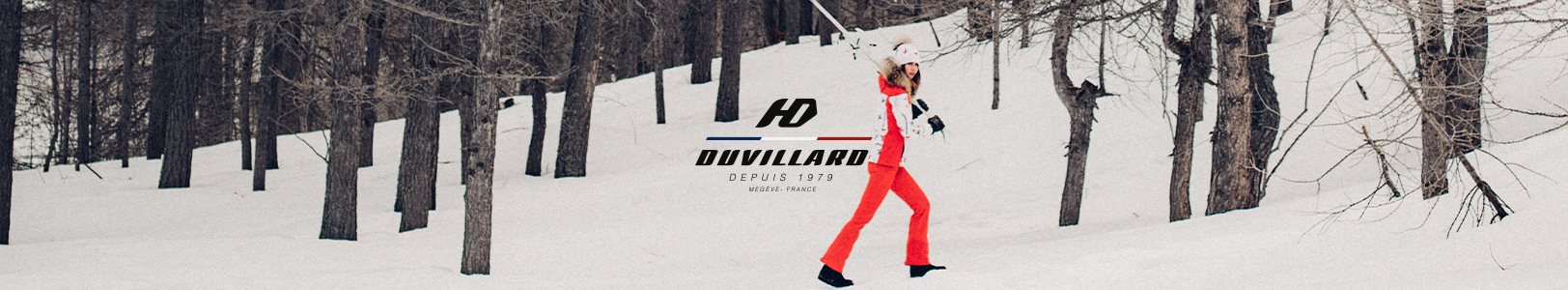 Henri Duvillard header image. A woman walking through the snow carrying skis wearing Henri Duvillard ski clothing