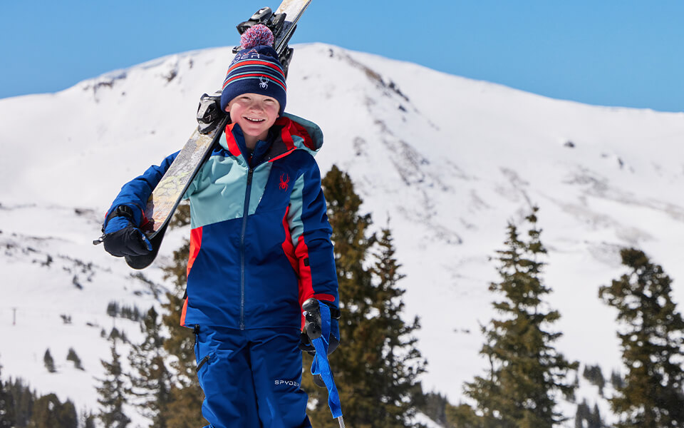 A child holding their skis in a Spyder ski jacket