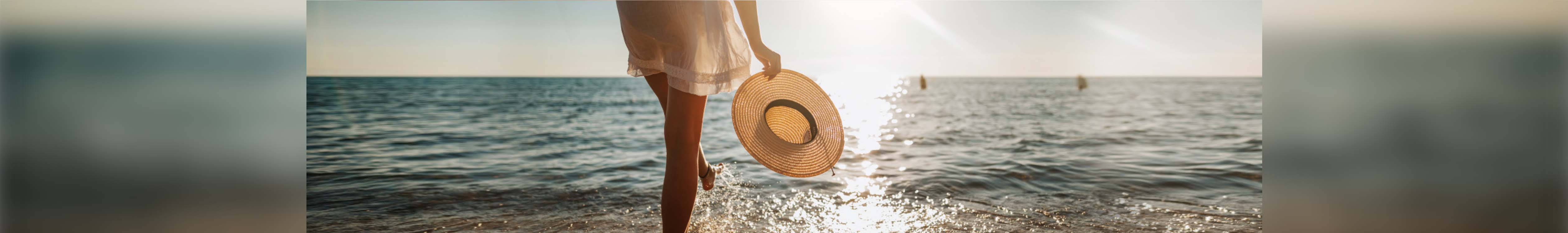 Beach holiday. A woman in a short white dress holding a straw hat walking in the sea 