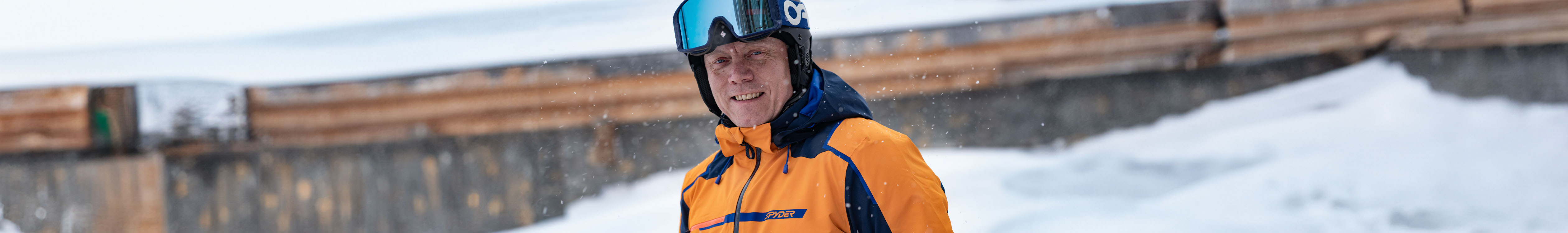 Man is smiling, wearing his ski jacket, ski helmet and goggles on top of his helmet