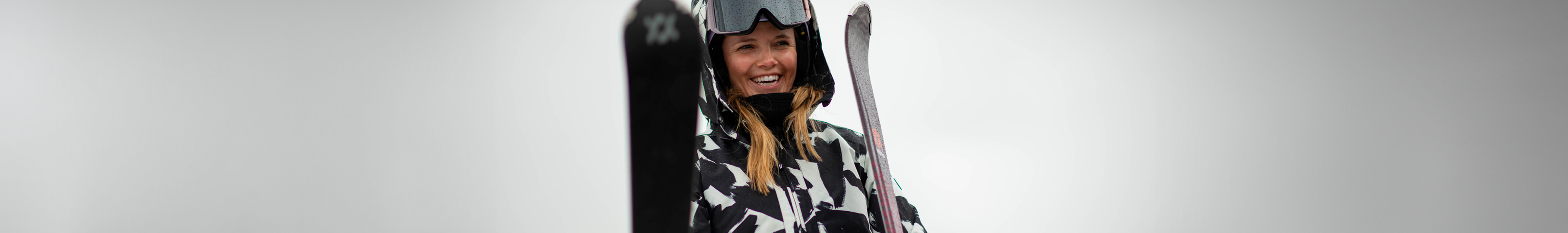 Woman is smiling and holding skies, wearing googles on top of her helmet