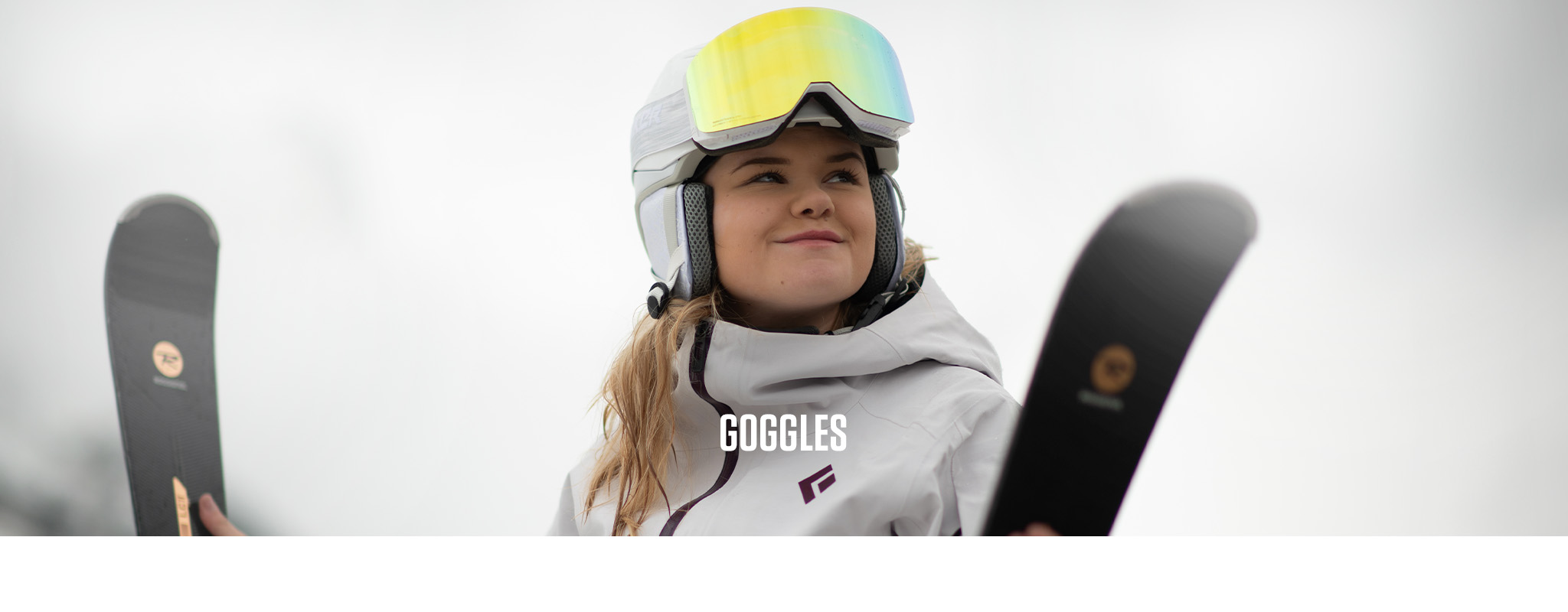 Shop goggles. A woman wearing orange ski goggles in front of a snowy backdrop 