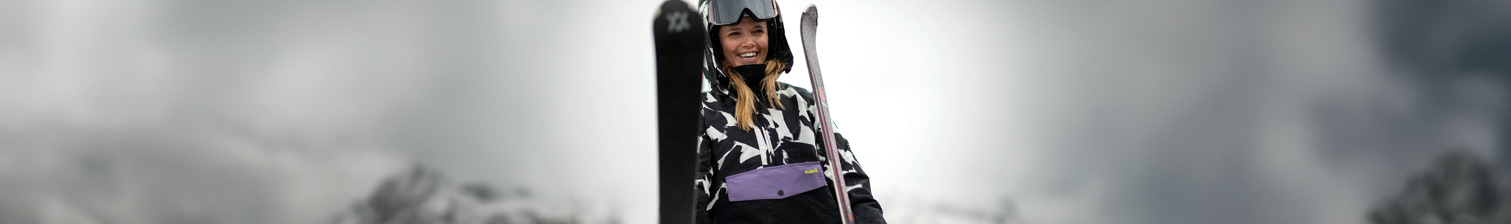 Gifts for skiers. A woman holding her skis in her skiwear, on a snowy mountain