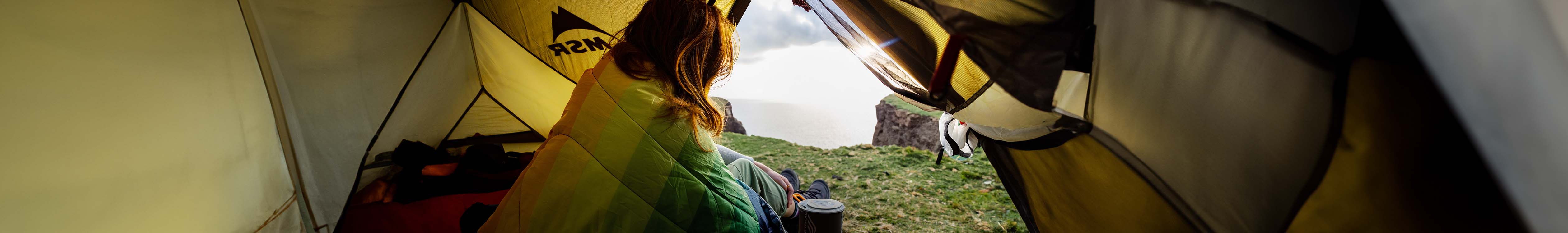 Camping new season. A woman is sitting in a tent with her legs being out and enjoying the view