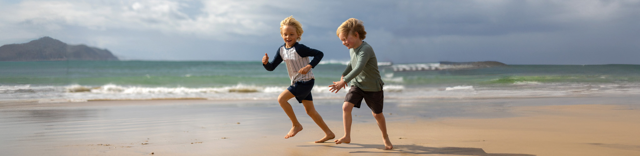 Kids' new season. Two children are running on the beach, wearing long-sleeved t-shirts and shorts