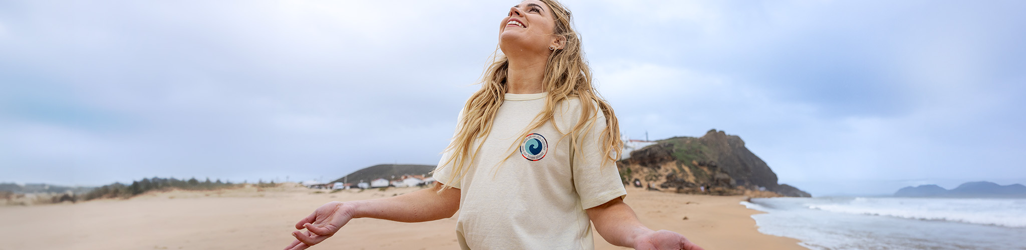 Women's summer styles. A woman is smiling and looking at the blue sky, wearing a white t-shirt on the beach