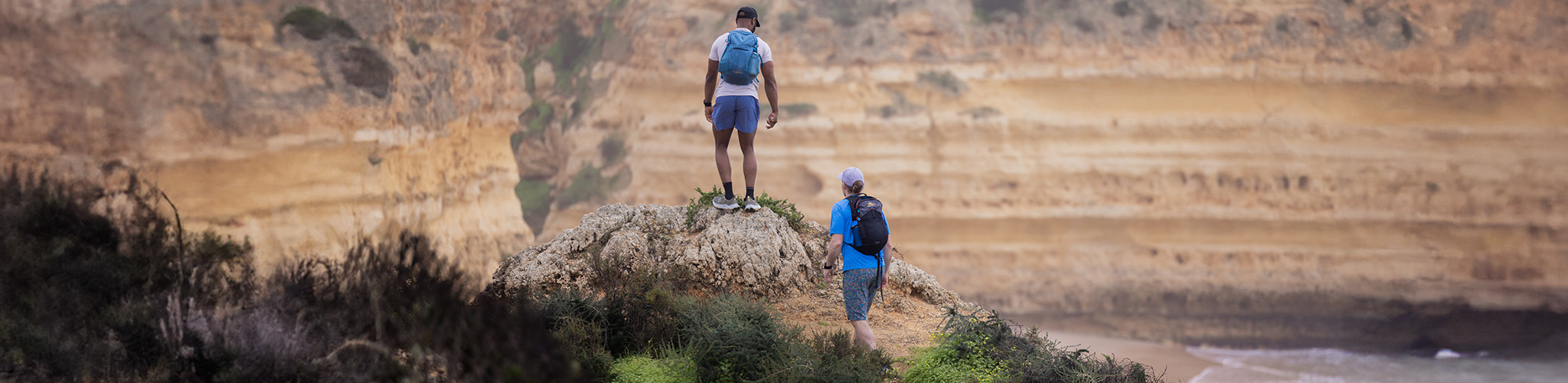 Shorts summer styles. Two men are hiking up, wearing t-shirts and shorts with backpacks somewhere warm