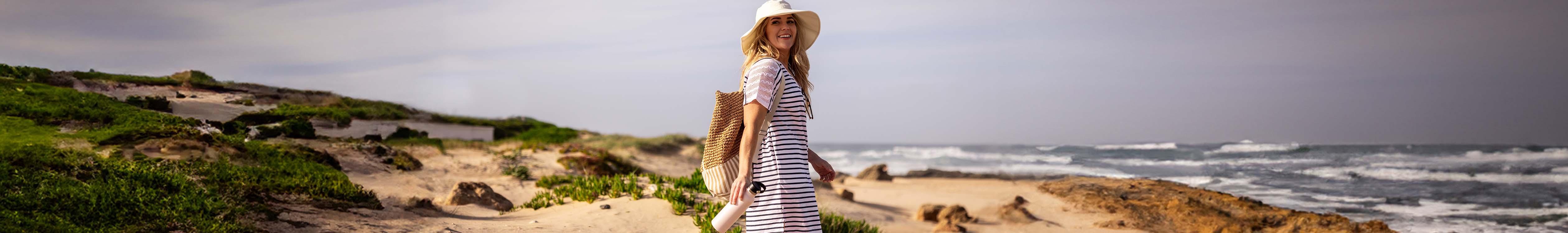 Shop dresses. A woman walking o a beach wearing a summer dress