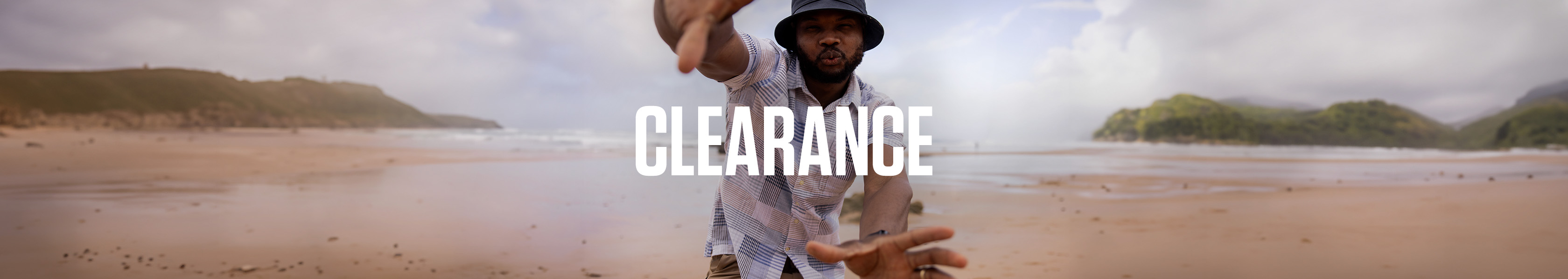 Shop Summer Clearnce. A man wearing summer shirt standing on a beach.