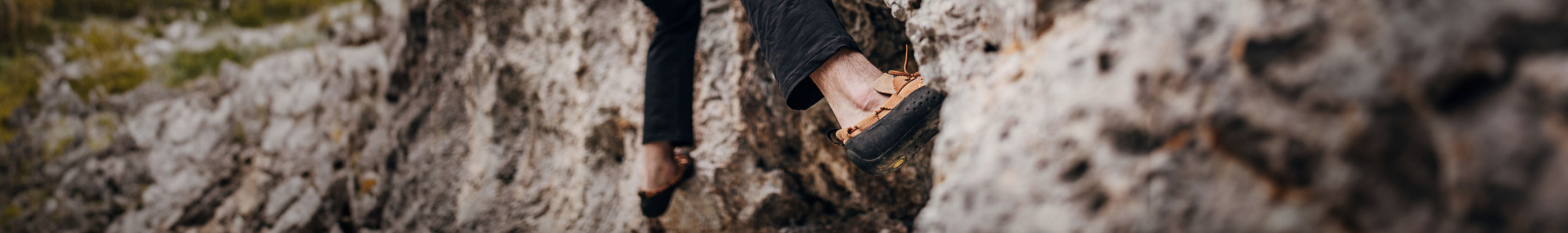 Shop Climbing Shoes. A person climbing a rock, wearing black legweare and climbing shoes