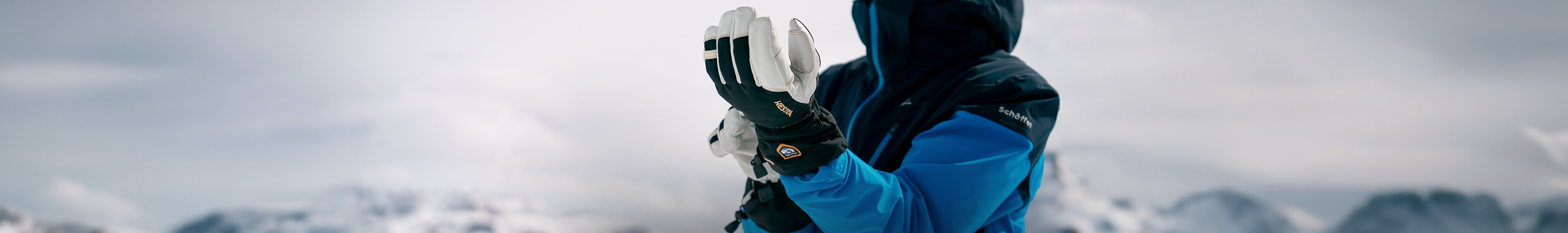 Shop snowboard accessories. Man standing on side of a snowy mountain adjusting his gloves