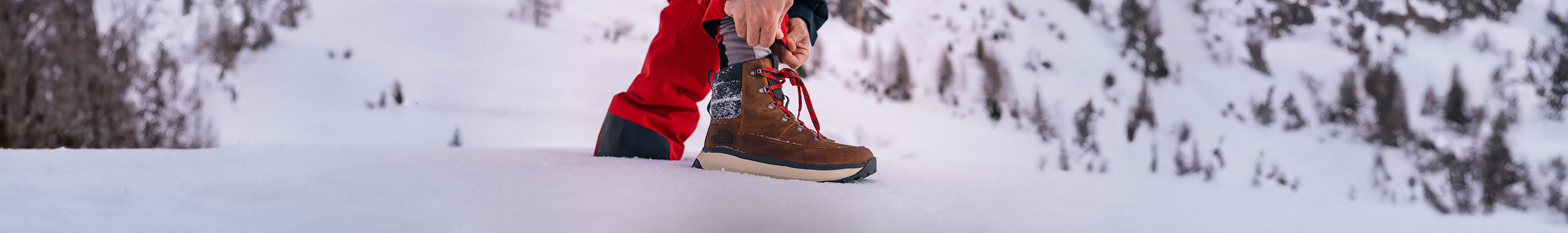 Shop snow boots,. Man tieing up laces on his snowboots