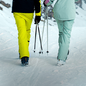 Shop snow pants. Two skiiers walking on the snow