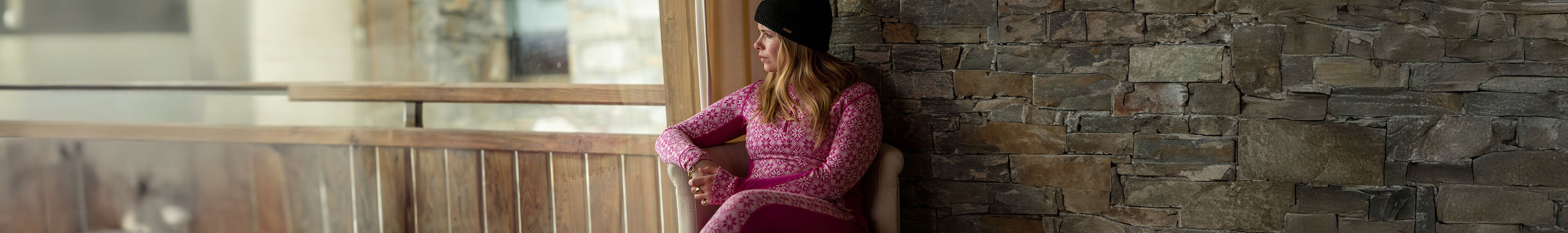 Shop bAselayers. A woman in pink pattern baselayer sitting by a window