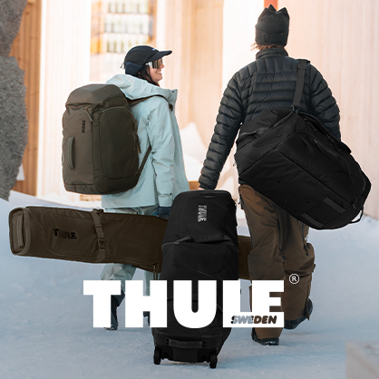 Shop Thule collection. Two people with backpacks and ski bags walking through snowy ski resort