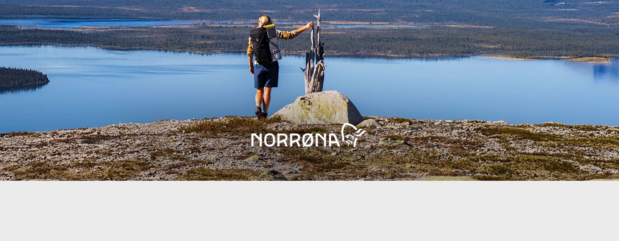 Shop Norrona collection. A person standing at the edge of a plain, looking at the lakes below