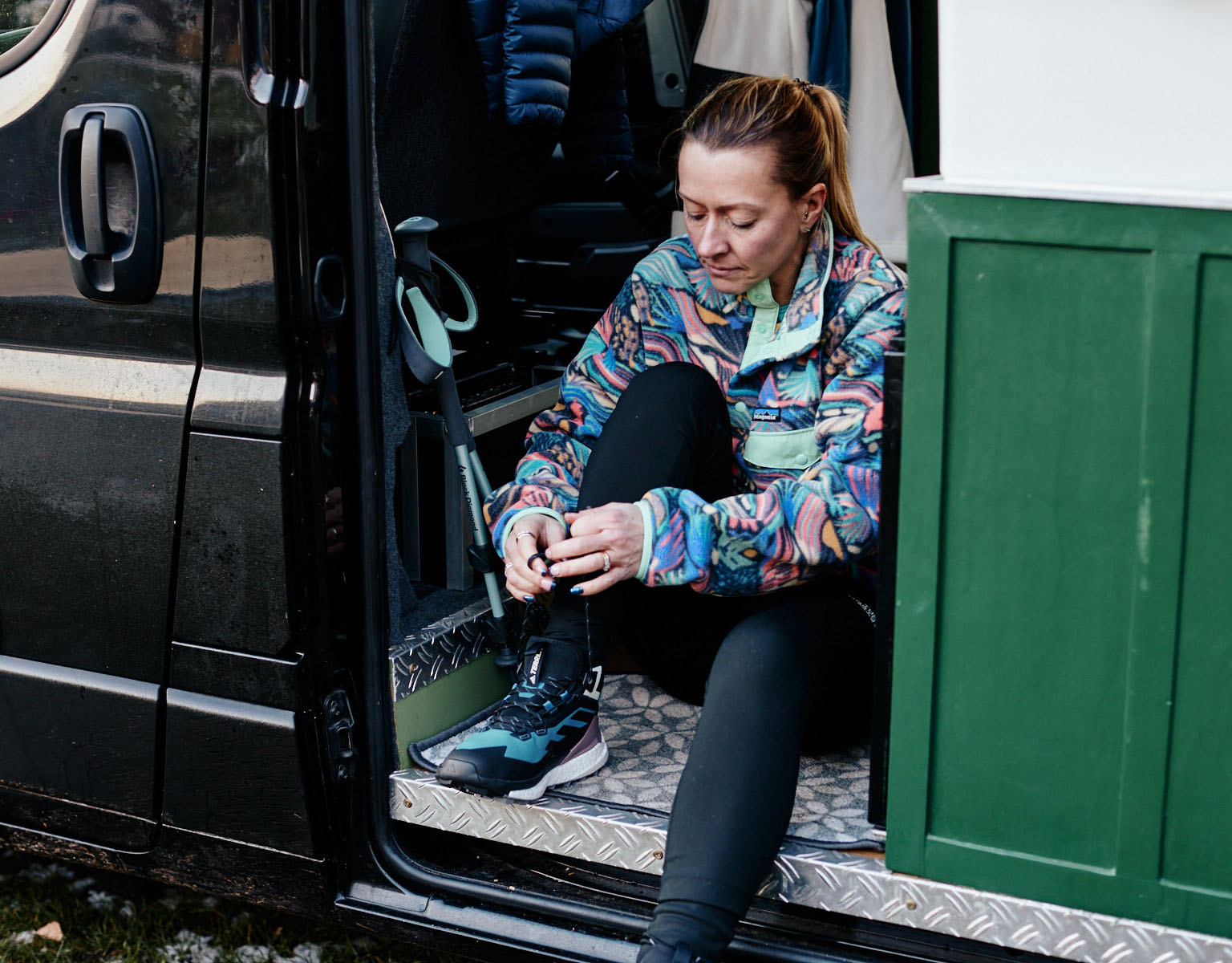 A woman is tieing shoe laces on a walking shoe in a van. 