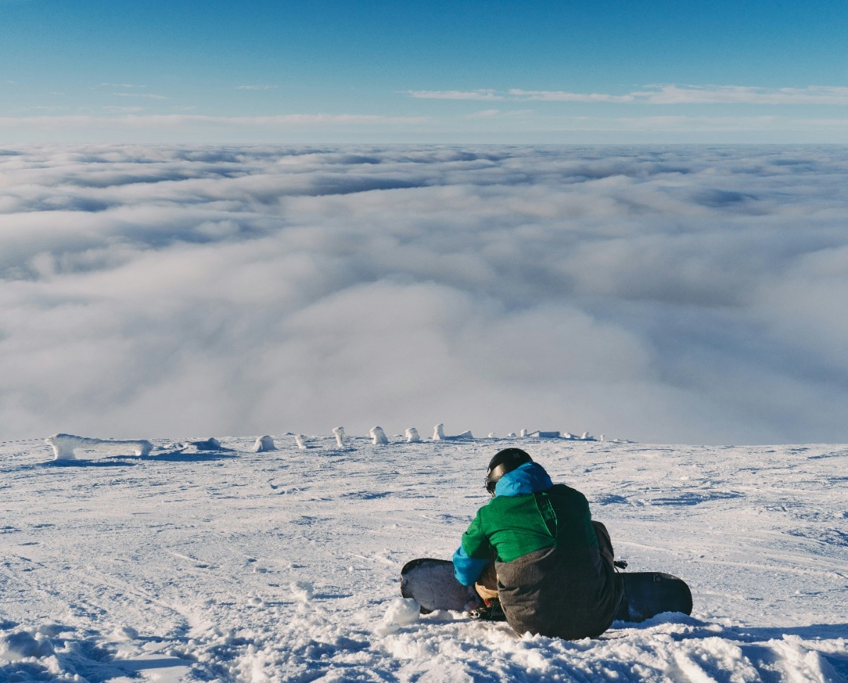 A man sat with his snowboard above the clouds at Jasna Ski Resort