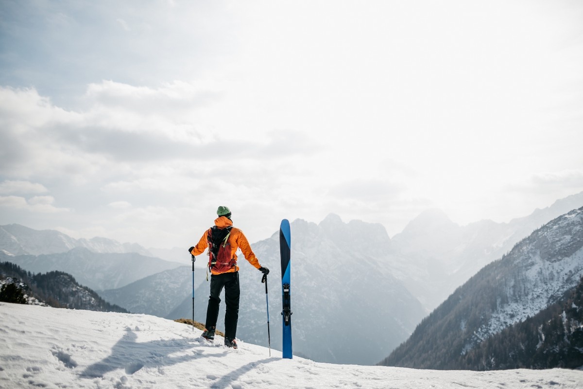 A man in a ski jacket staring out across the mountains with his skis 