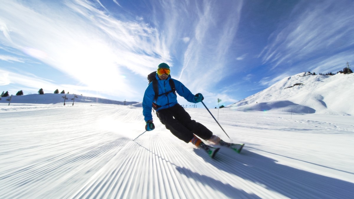 A man skiing in a blue ski jacket down a fresh piste