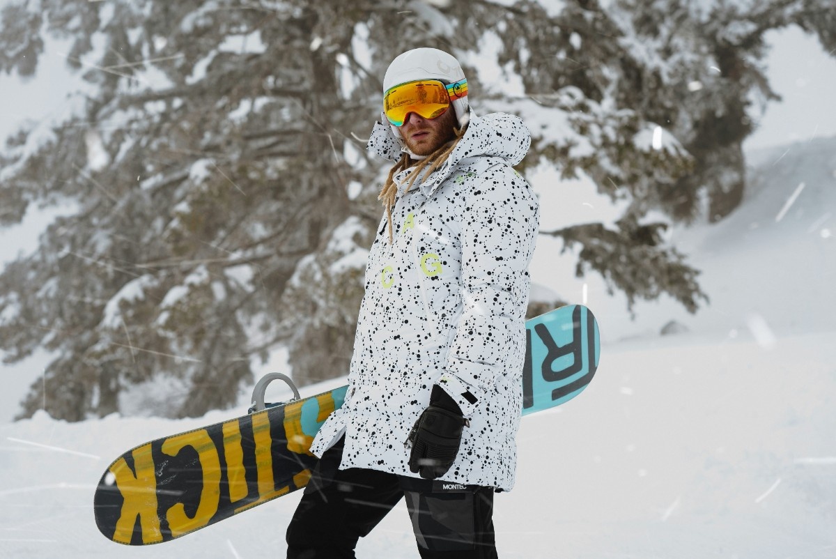 A person wearing ski mitts holding a snowboard in the snow 